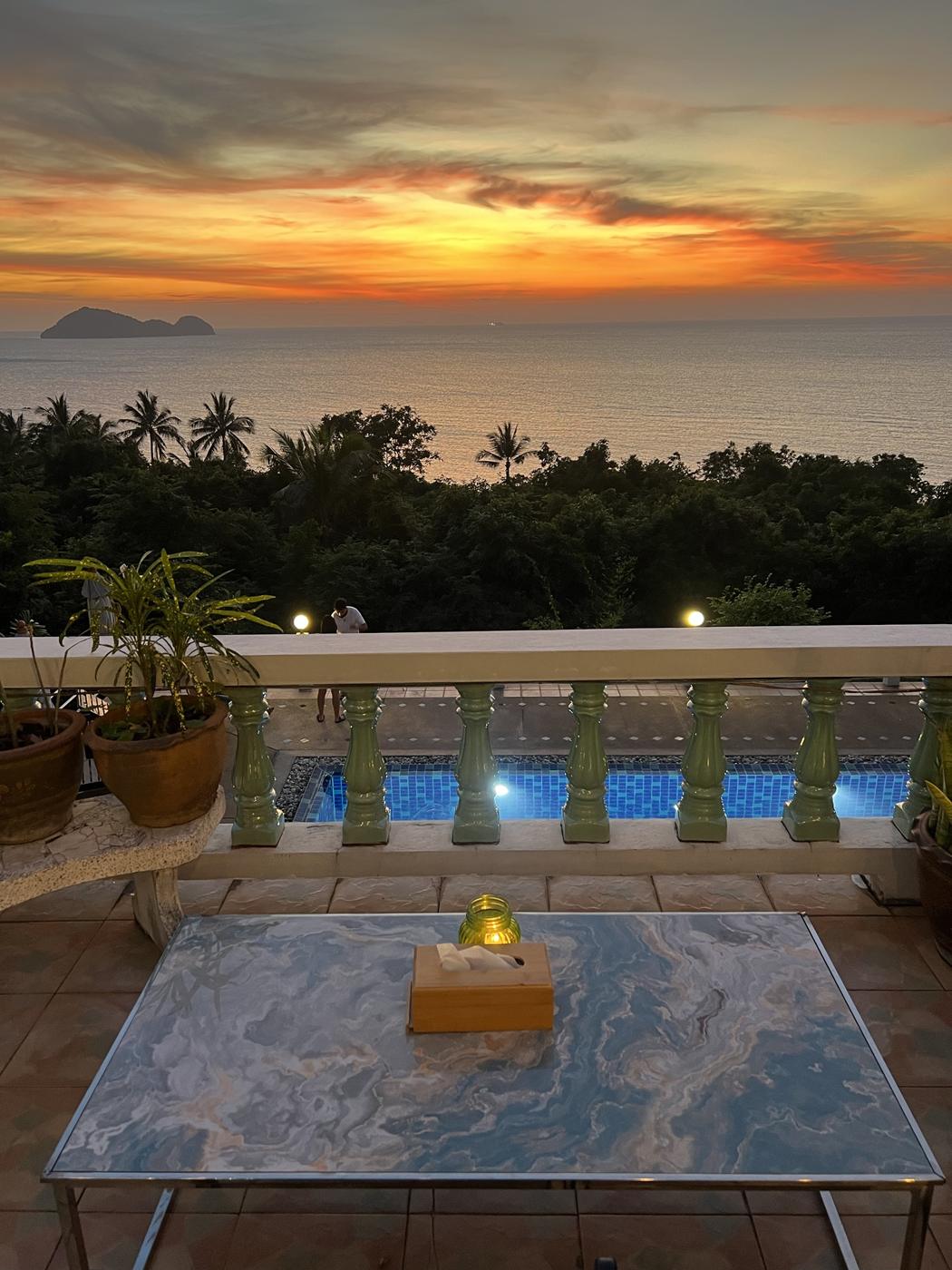 Candle on a terrace table above the pool at sunset