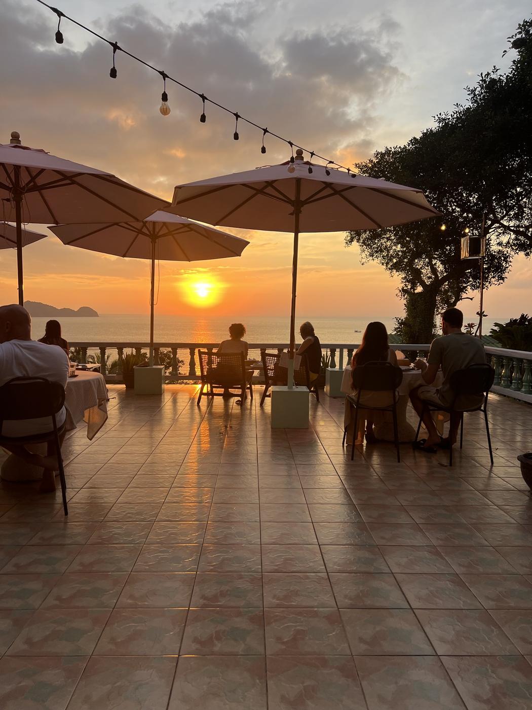 Guests dining under umbrellas on the Mille terrace at sunset